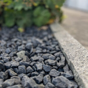 Svart Diabas Tumlad längs kantsten och plantering i trädgårdsmiljö